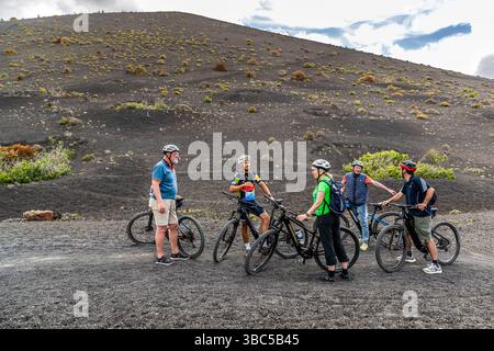 Eine Gruppe von Radfahrern macht eine Pause am Fuße eines schwarzen Vulkankonuses im vulkanischen Gelände von Lanzarote. LZ-56, Tegoyo, Kanarische Inseln, Spanien. Stockfoto