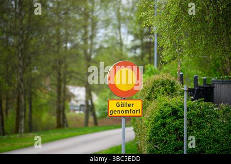 Ein leuchtend gelbes und rotes Schild warnt vor einer unerlaubten Durchfahrt. Es befindet sich in der Nähe einer gewundenen Straße, die von lebhaftem Grün gesäumt ist, in einer friedlichen Landschaft Stockfoto
