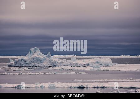 In der Baffin Bay, Westgrönland, treiben Eisschollen unter einem bewölkten arktischen Himmel. Eine stimmungsvolle und entfernte Polarszene, die Meereis in Schichten zeigt. Stockfoto