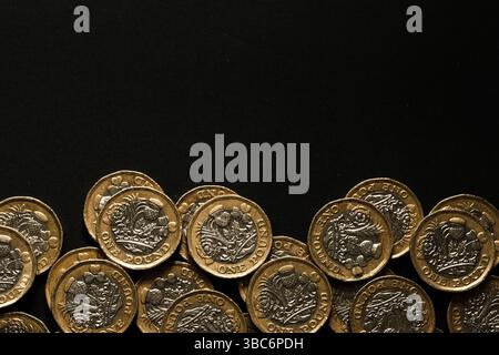 Verstreute britische ein-Pfund-Münzen, die am Boden eines schwarzen Hintergrunds gesäumt sind, symbolisieren Sparsamkeit, Reichtum und britische Währung, Stafford, Vereinigtes Königreich Stockfoto