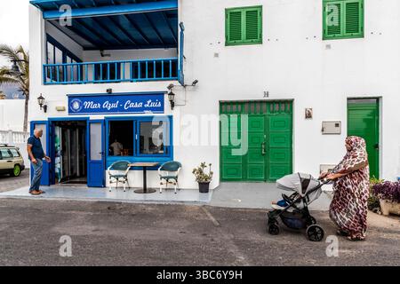 El Golfo auf Lanzarote: Ein Mann steht vor dem Restaurant „Mar Azul - Casa Luis“ und eine Frau schiebt einen Kinderwagen. Avenida Marítima, El Golfo, Canarias, Spanien Stockfoto