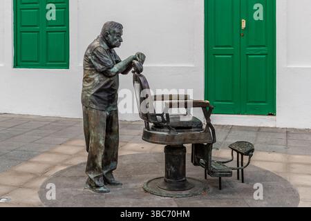 Bronzestatue von Ladislao Rodriguez Bonilla, dem berühmten Friseur in der Stadt Haria auf Lanzarote, an einem Friseurstuhl stehend. Sogar das spanische Königspaar hat seinen Friseur besucht. Plaza de la Constitución, Haría, Canarias, Spanien Stockfoto
