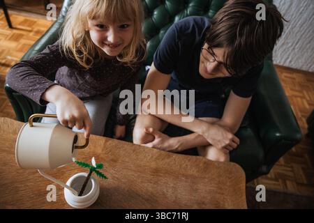 Kinder können im Innenbereich kreative Gartenarbeit betreiben, indem sie eine Wasserkanne und eine Pflanze verwenden Stockfoto