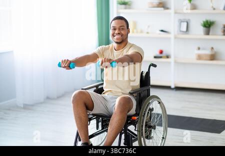 Rehabilitation von behinderten Menschen. Junger afroamerikanischer Mann im Rollstuhl, der zu Hause arbeitet Stockfoto