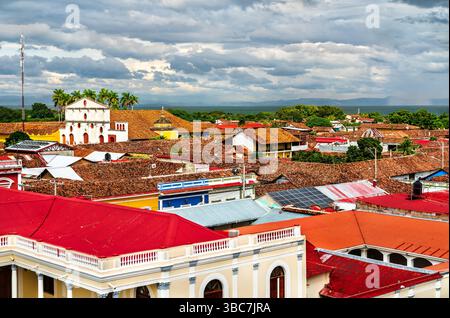 Malerischer Blick über die rot gekachelten Dächer von Granada, Nicaragua, mit der farbenfrohen Kolonialarchitektur der Stadt und der üppigen nicaraguanischen Landschaft unter einem dramatischen Himmel Stockfoto