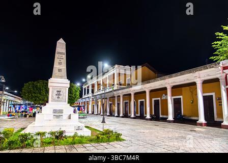 Granada, Nicaragua - 1. Dezember 2024: Nächtlicher Blick auf das Unabhängigkeitsdenkmal an der Plaza de la Independencia in Granada, beleuchtet mit umliegender Kolonialarchitektur und Straßenmarkt. Das Denkmal ehrt die nicaraguanischen Helden von 1811 und erinnert an die Unabhängigkeit des Landes im Jahr 1821 Stockfoto