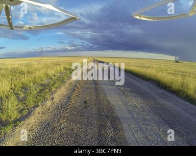 Aus der Vogelperspektive von einer Landungsdrohne auf einer unbefestigten Straße im Pawnee National Grassland mit Windmühle und Bohrinsel Stockfoto
