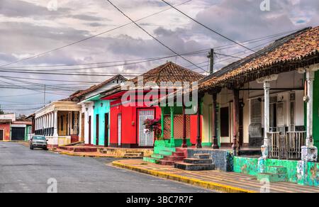 Eine Reihe von lebhaften Häusern im Kolonialstil mit kunstvollen Balkonen, Bogenfenstern und üppigem Grün säumt eine enge Kopfsteinpflasterstraße in Granada, Nicaragua. Die Pastellfarben und architektonischen Details spiegeln den Charme und die Geschichte des gut erhaltenen kolonialen Erbes der Stadt wider Stockfoto