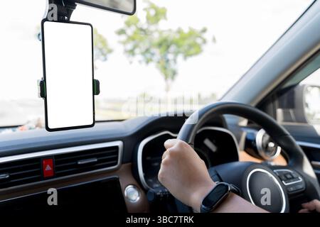 Nahaufnahme der Hand des Fahrers am Lenkrad und Smartphone mit leerem Bildschirm auf dem Armaturenbrett des Fahrzeugs, Konzept für Navigation, Technologie, Straßenverkehrssicherheit, Stockfoto