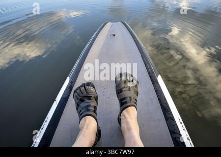 Man Füße in fünf Fingern Wasserschuhen auf einem Stand Up Paddleboard Stockfoto