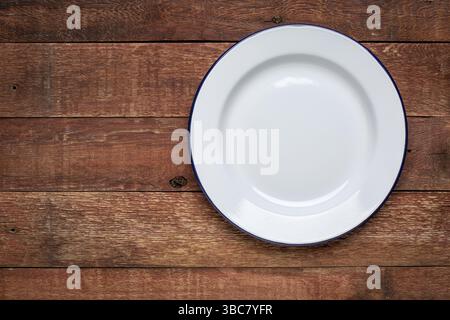 Leere weiße Emaille-Platte aus Metall auf rustikalem Holz mit Kopierraum Stockfoto