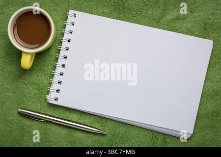 Leeres spiralförmiges Kunstskizzenbuch auf grün strukturiertem Rindenpapier mit einer Tasse Kaffee Stockfoto