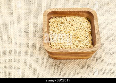Goldene Flachssamen in quadratischer Holzschale gegen Sackleinen Stockfoto