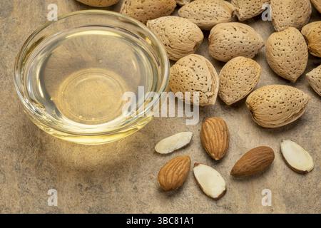 Mandelnüsse und Öl in einer kleinen Glasschale über strukturiertem Rindenpapier Stockfoto