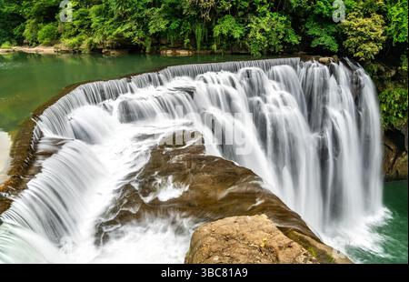 Der Shifen Wasserfall im Pingxi District in New Taipei, Taiwan, stürzt sich in einen türkisfarbenen Pool inmitten von dichtem Grün und bietet eine malerische und ruhige natürliche Attraktion, die oft als Little Niagara von Taiwan bezeichnet wird Stockfoto