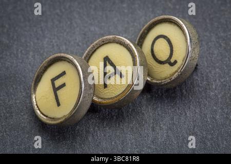 FAQ (häufig gestellte Fragen) Akronym in alten runden Schreibmaschinenschlüsseln gegen grauen Schieferstein Stockfoto