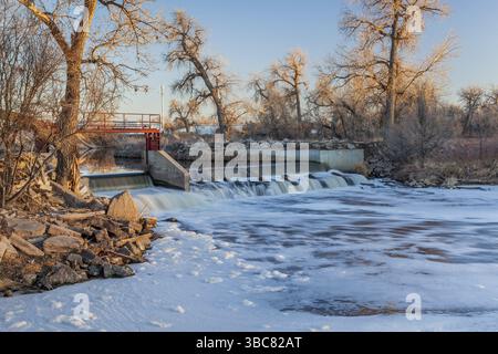 Kleiner Flussdamm, der Wasser zur Bewässerung von Ackerland umleitet - South Platte River in der Nähe von Fort Lupton, Colorado, Winterlandschaft bei Sonnenuntergang Stockfoto