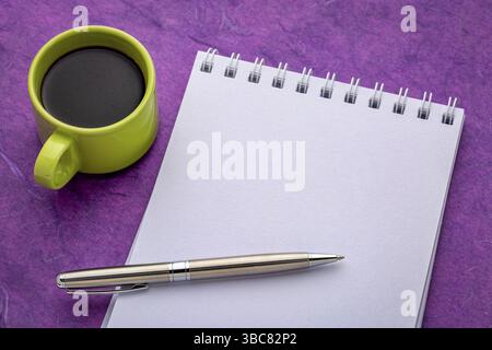 Leeres spiralförmiges Kunstskizzenbuch auf lila strukturiertem Rindenpapier mit einer Tasse Kaffee Stockfoto