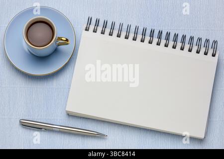 Leeres spiralförmiges Kunstskizzenbuch mit einer Tasse Kaffee gegen strukturiertes Krepppapier Stockfoto