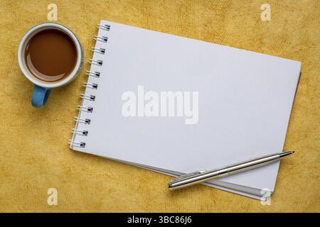 Leeres spiralförmiges Kunstskizzenbuch auf gelb strukturiertem Rindenpapier mit einer Tasse Kaffee Stockfoto
