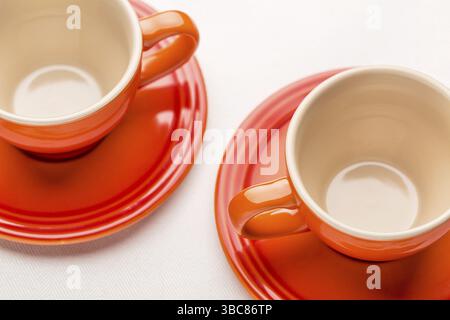 Zwei leere Steingut-Kaffeetassen gegen weiße Tischdecke, geringe Tiefe der Feile Stockfoto