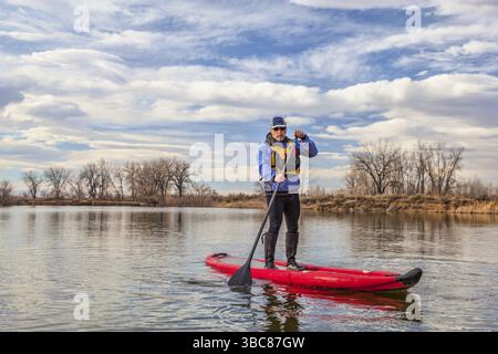Senior man paddelt ein aufblasbares Stand Up Paddleboard auf einem See im Herbst oder Winter in Colorado Stockfoto