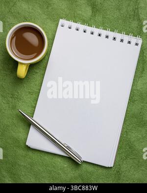 Leeres spiralförmiges Kunstskizzenbuch auf grün strukturiertem Rindenpapier mit einer Tasse Kaffee Stockfoto
