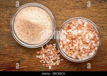 Feine und grobe Kristalle aus rosa Himalaya-Salz in Glasschalen auf rustikalem Holz, Blick von oben Stockfoto
