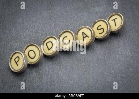 Podcast-Wort in alten runden Schreibmaschinenschlüsseln gegen grauen Schieferstein Stockfoto