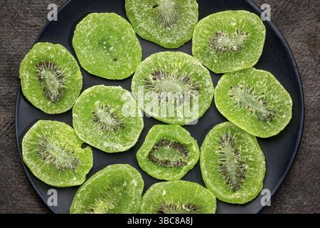 Scheiben getrockneter Kiwis auf einer schwarzen Platte gegen strukturiertes, handgefertigtes Rindenpapier Stockfoto