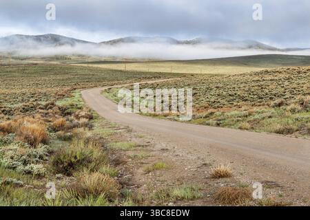 Unbefestigte Straße in einem Bergtal mit Hügeln, die am frühen Frühlingsmorgen von Sagebrush bedeckt sind, North Park, Colorado Stockfoto