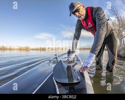 Der ältere Paddler mit aufblasbarer Schwimmweste und Paddelhandschuhen wirft sein Stand Up Paddleboard auf einem See ab, Bild mit Action-Kamera Weitwinkel Stockfoto
