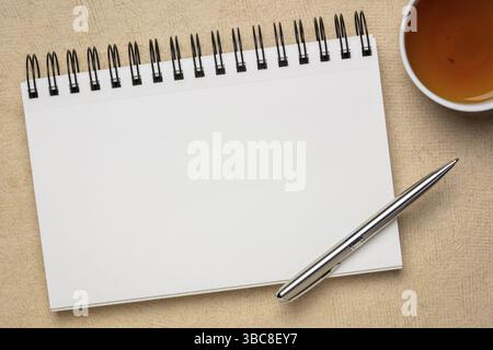 Leeres spiralförmiges Kunstskizzenbuch gegen strukturiertes Rindenpapier mit einer Tasse Tee Stockfoto