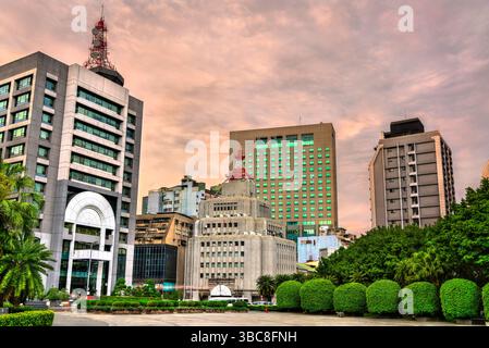 Skyline des Ximending Viertels in Taipeh, Taiwan bei Sonnenuntergang, mit einer Mischung aus modernen Gebäuden und Gebäuden aus der Mitte des Jahrhunderts, umgeben von üppigem Grün und einem farbenfrohen Himmel. Markante Türme erheben sich über dem dichten städtischen Gefüge und spiegeln die architektonische Vielfalt der Hauptstadt Taiwans wider. Stockfoto