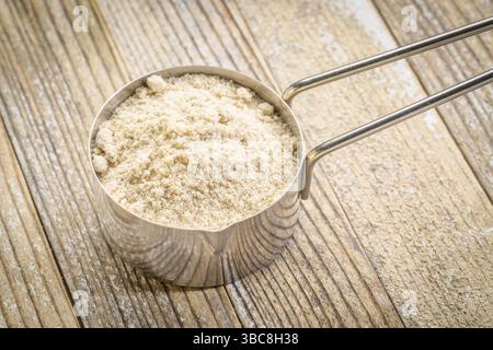 Molkenproteinpulver in einem Metallmesslöffel vor Grunge-Holzhintergrund Stockfoto