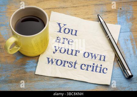 Sie werden Ihre eigenen schlimmsten Kritiker - Handschrift auf einer Serviette mit einer Tasse Espressokaffee Stockfoto