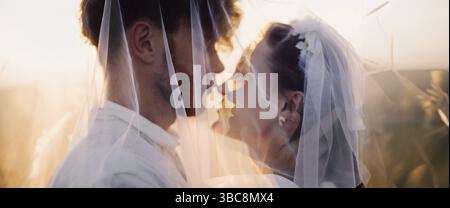 Silhouette eines romantischen Brautpaares mit Schleiern vor Sonnenuntergang Stockfoto