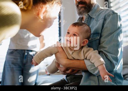 Ältere Schwester, die den neugeborenen Bruder im Arm des Väters ansieht. Stockfoto