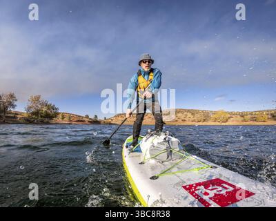 Fort Collins, CO, USA - 15. Oktober 2019: Ein älterer Mann paddelt auf einem aufblasbaren Stand Up Paddleboard von Red Paddle Co gegen Gegenwind auf dem Bergsee Stockfoto