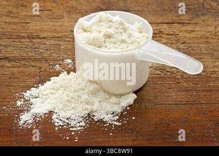 Kunststoff-Messlöffel mit weißem Pulver (Molkenprotein) vor Grunge-Holz-Hintergrund Stockfoto