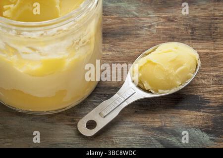 Glas und Messlöffel Ghee - geklärte Butter auf Grunge-Holz Stockfoto