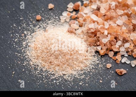 Feine und grobe Kristalle von rosa Himalaya-Salz auf grauem Schieferstein Stockfoto
