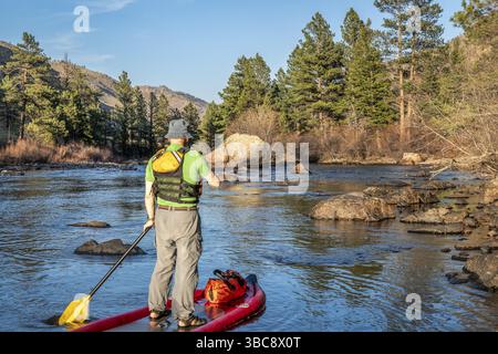 Aufblasbares Stand-Up-Paddleboard für ältere Männer durch einen Steingarten auf einem Bergfluss - Poudre River in Colorado in Frühlingslandschaft mit niedrigen W Stockfoto