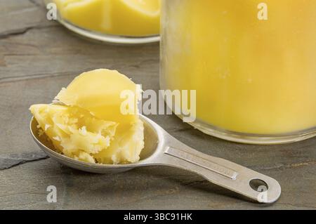 Dosensand, der Esslöffel Ghee misst - geklärte Butter auf Grunge-Holz Stockfoto
