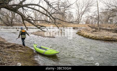 Männlicher Paddler zieht sein aufblasbares Wildwasser-Kajak flussaufwärts auf einem flachen Schnellboot - dem Poudre River in Fort Collins, Colorado, in der Frühjahrslandschaft Stockfoto