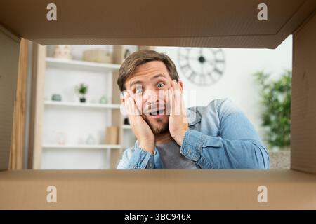 Ein überraschter Mann packt den aufklappbaren Karton aus Stockfoto