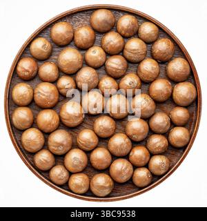Macadamia-Nüsse in Schalen auf einem runden Holztablett isoliert auf weiß Stockfoto