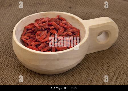 Getrocknete tibetische Goji-Beeren (Wolfsbeeren) auf einer rustikalen unfertigen Holzschaufel, Sackleinen Hintergrund Stockfoto