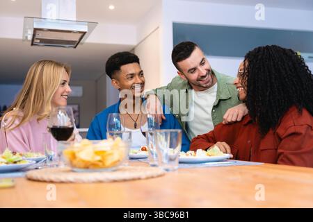 Multiethnische Gruppe von Freunden, die Abendessen und Unterhaltung am Heimtisch genießen Stockfoto