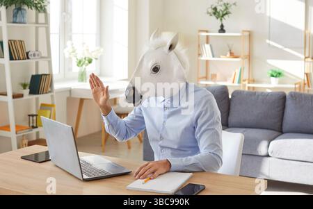 Lustiger extravaganter glücklicher Mann mit Esel, Pferdekopf, der auf den Computerbildschirm blickt und hallo winkt Stockfoto